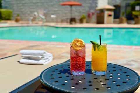 Colorful cocktails on poolside table with resort pool and umbrellas in background