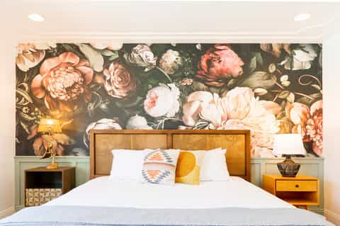 Bedroom with rattan headboard, floral wall mural, white bedding, and warm decorative lighting