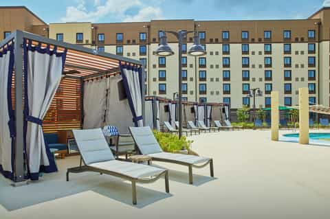 Outdoor resort deck with navy cabanas, lounge chairs, large hotel building, and blue pool water visible