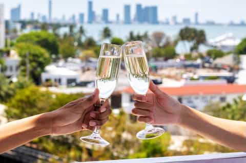 Two champagne glasses clinking with city skyline blurred in background, celebrating at an elevated venue