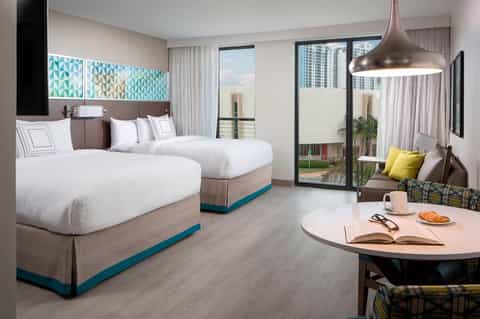 Modern hotel room with two queen beds, blue accents, flat-screen TV, and balcony overlooking city skyline