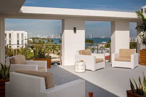 Waterfront terrace with white chairs, ocean and city skyline views through large windows