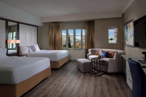 Spacious hotel room with two queen beds, sitting area, and city view windows