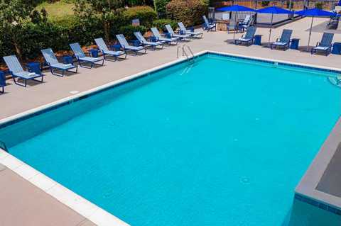Resort pool with turquoise water, striped loungers, blue umbrellas, and landscaped surroundings