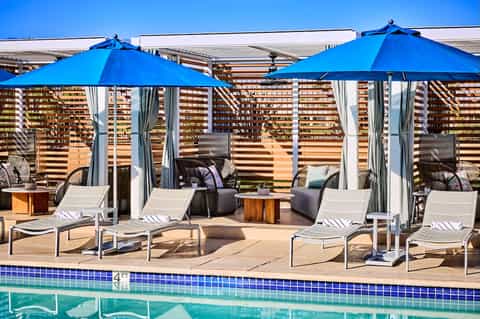 Pool deck with blue umbrellas, loungers, and wooden privacy screens