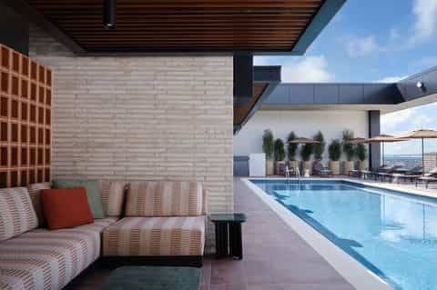 Striped modern seating area beside rectangular pool with white walls, potted plants, and lounge chairs