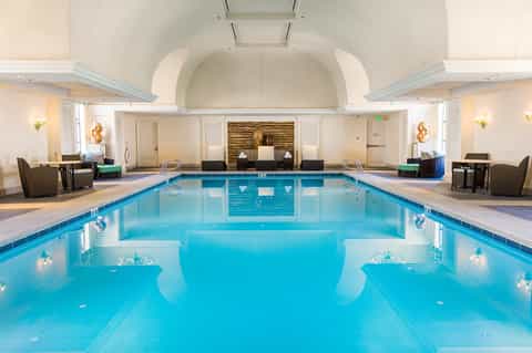 Indoor hotel pool with arched ceiling, blue water, cream-colored architecture, and ambient lighting