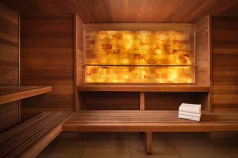 Wooden sauna interior with illuminated stone wall and white towels on bench
