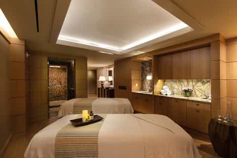 Luxury spa treatment room with massage beds, wood paneling, and ambient lighting