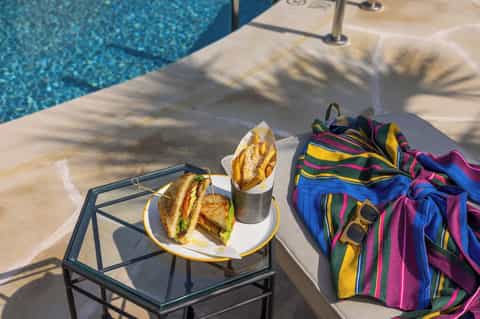 Poolside lunch with sandwich, drink, and colorful striped beach towel