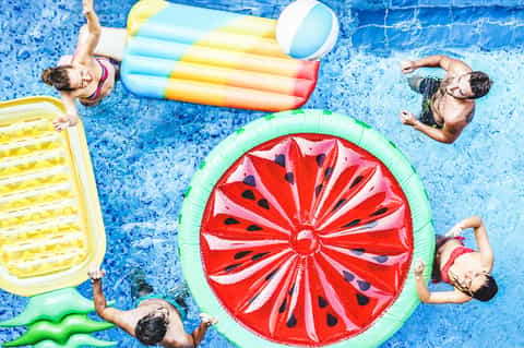 Overhead view of children on colorful pool floats in bright blue swimming pool