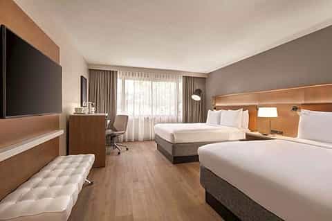 Modern hotel room with two queen beds, wood accents, and contemporary furnishings