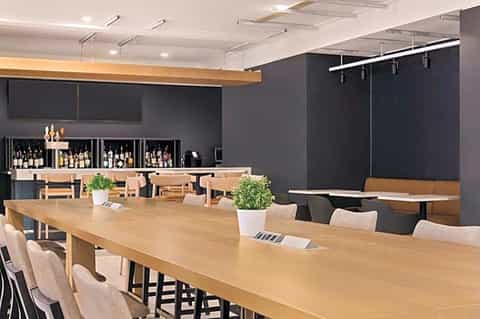 Modern meeting room with wooden conference table, bar with wine bottles, and dark accent wall