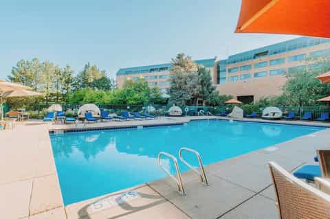 Resort pool with blue loungers, orange umbrellas, and modern building with glass architecture