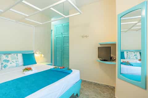 Colorful hotel room with turquoise accents, double bed, flat-screen TV, and bright ceiling