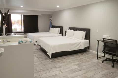 Modern hotel room with two queen beds, black headboards, white bedding, desk area, and bathroom