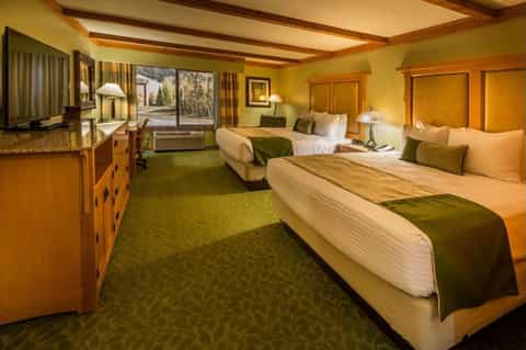Spacious hotel room with two queen beds, green accents, wooden furniture, and patio doors