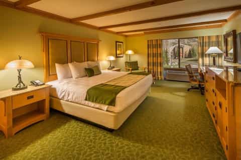 Hotel bedroom with yellow walls, wooden furniture, green accents, and large windows overlooking grounds