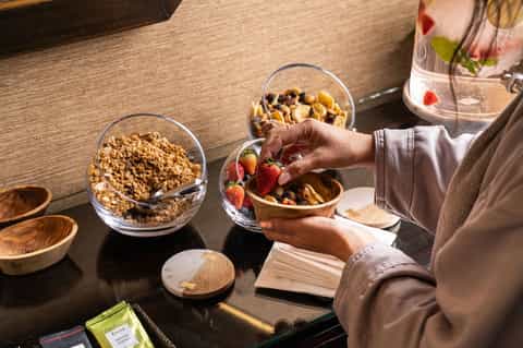 Person eating healthy breakfast with granola, fruit, nuts, and beverage