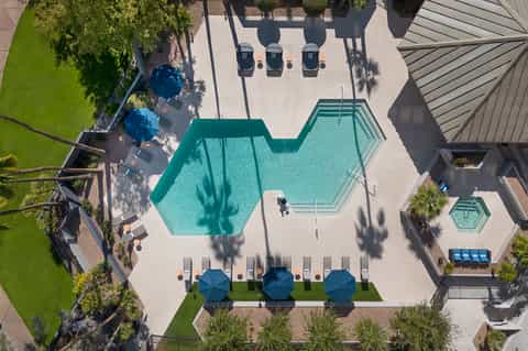 Aerial view of resort pool complex with hexagonal pools, umbrellas, lounge chairs, and landscaping