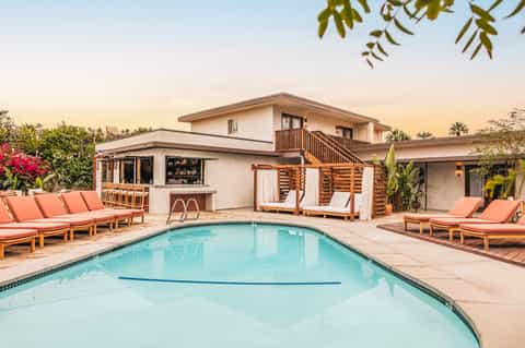 Modern residential pool with coral lounge chairs, bar area, and contemporary architecture at sunset