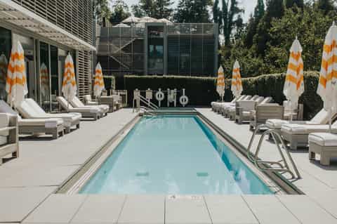 Modern resort lap pool with geometric white umbrellas, lounge chairs, hedges, and contemporary architecture