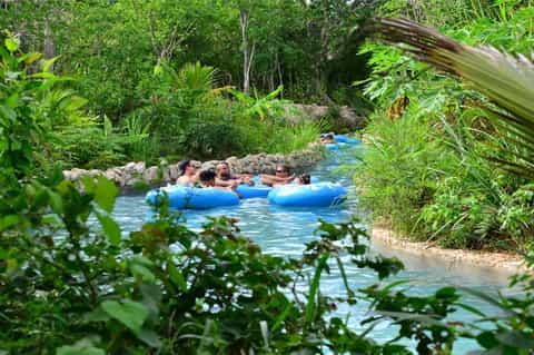 Natural hot spring with geothermal blue water, people floating on tubes, surrounded by dense tropical vegetation