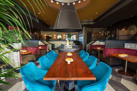 Contemporary dining space with colorful blue chairs, wooden table, fireplace, and vibrant accent lighting