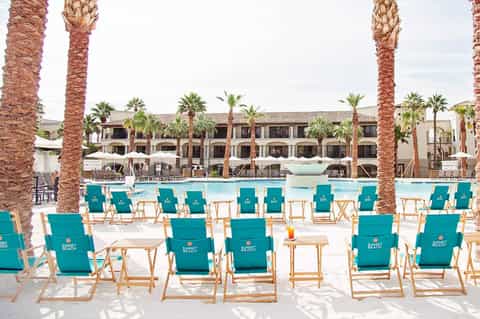 Resort pool area with turquoise lounge chairs, palm trees, and beachfront hotel building