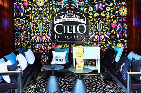 Vibrant lounge space with colorful floral wallpaper, El Diamante del Cielo Tequila branding, blue seating, and decorative pillows