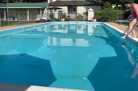 Residential community pool with crystal blue water, white diving board, cottages, and green lawn areas