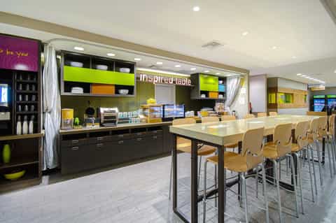 Hotel breakfast room with green accents, counter service, and high-top seating areas