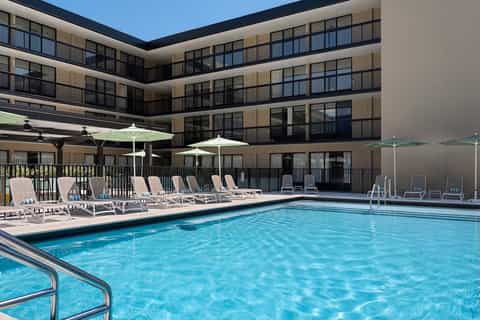 Courtyard pool area surrounded by multi-story hotel building with loungers and umbrellas
