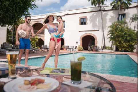 Family playing by resort swimming pool with historic colonial building and palm trees