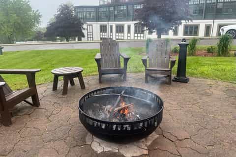 Outdoor fire pit seating area with Adirondack chairs on grass near modern building