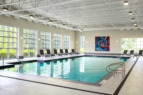 Indoor heated pool with lounge chairs, large windows, and modern facility design