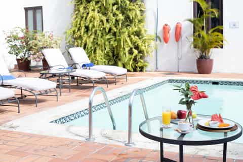 Small resort pool with lounge chairs, potted plants, and white building facade