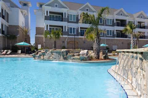 Luxury waterfront resort with white buildings, decorative pool with rock features, and palm trees