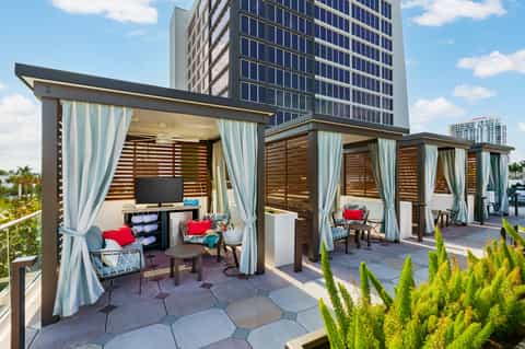 Urban rooftop cabanas with white curtains, wooden slats, and city skyline views