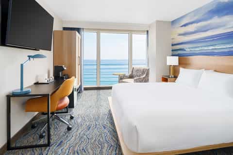 Beachfront hotel room with ocean view balcony, desk workspace, and modern furnishings