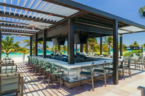 Beachfront bar with pergola seating, ocean view, palm trees, and modern architecture