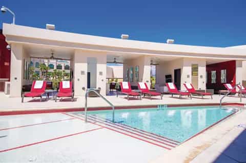 Hotel pool with pink and white loungers on covered patio near facility building