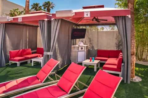 Resort cabana pods with red furnishings, curtains, lounge chairs, and manicured lawn