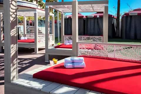 Outdoor daybed cabanas with red cushions under pergola shade structures and landscaping