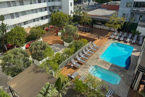 Rooftop resort pool area with lounge chairs, striped umbrellas, wooden decking, and modern apartment buildings