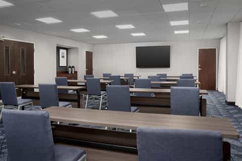 Corporate conference room with long wood table, blue chairs, and wall-mounted screen