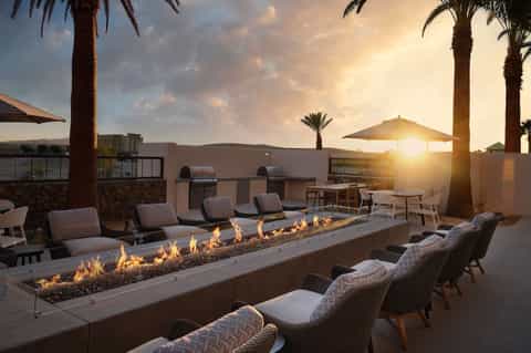 Rooftop terrace with dual linear fire pits, wicker lounge chairs, and sunset desert landscape