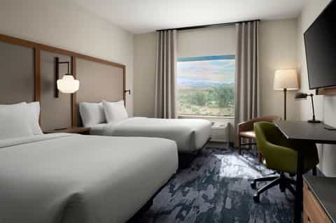Modern hotel room with two queen beds, wooden frames, floor-to-ceiling window, and scenic desert view