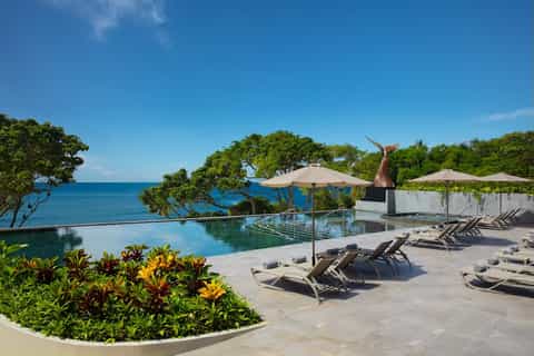 Infinity pool overlooking ocean with tropical vegetation and loungers