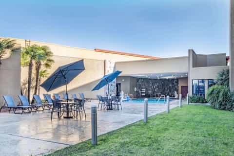 Modern resort pool area with blue umbrellas, lounge chairs, white walls, and landscaped grounds